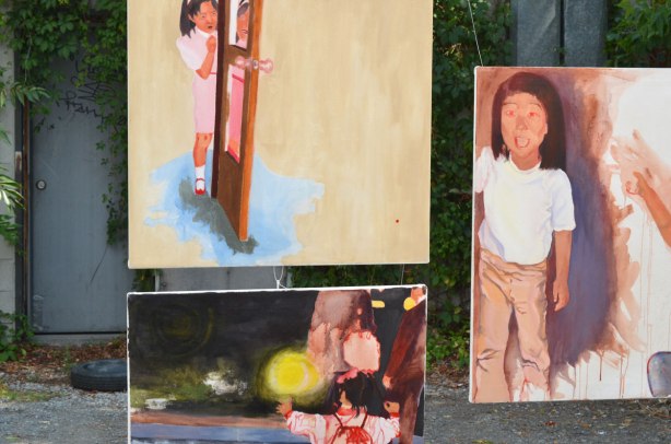 Parts of three paintings of children hanging outside on display 
