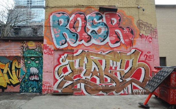 rasr tag on the upper story of a building in an alley . another tag under it that also covers a door. 