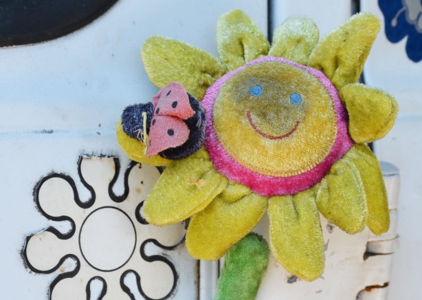 old and faded and dirty yellow fabric flower with a happy face on it. 