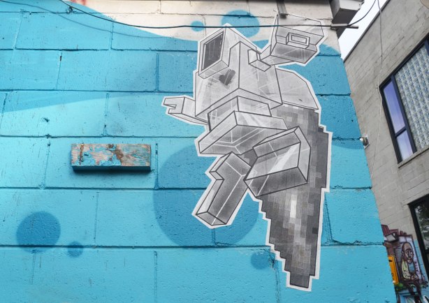 large wheatpaste lovebot on a wall that's been painted sky blue. 3D lovebot looks like he's running or jumping. 