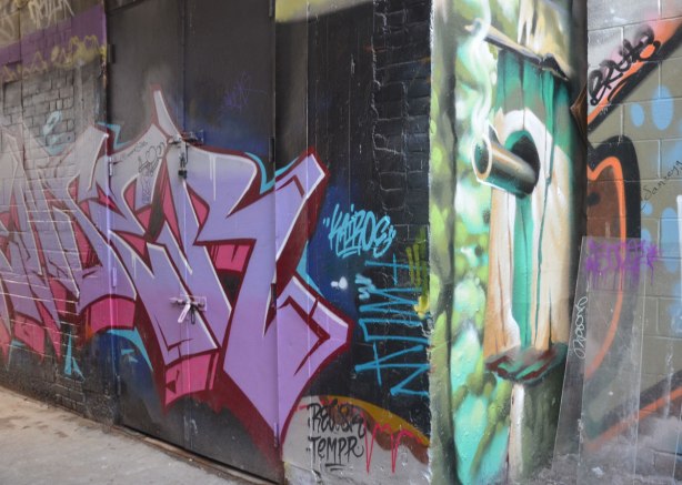 Narrow street art painting of a smoking gun sticking out of a hole in a wall. 