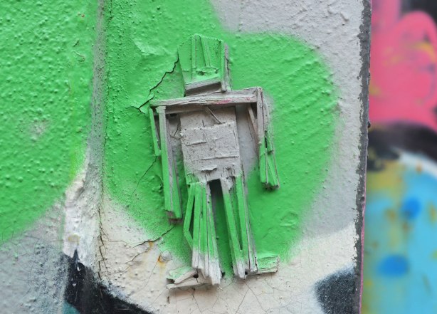 Stickman on a wall with green and grey spray paint on top of him and around him