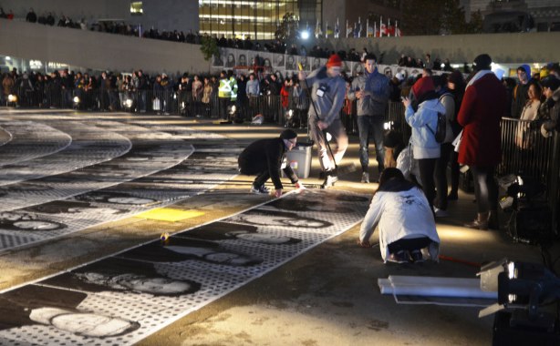 a group of people is gluing pictures to the concrete while many people look on, most are behind barricades, night time 