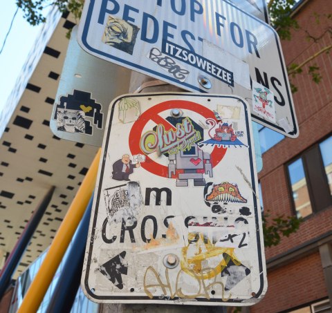 street signs covered with stickers and slaps in front of OCAD University