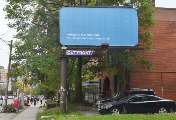 a billboard on a city street. it is blue with just the words on it that say Refugees run the seas cause we own our own votes 