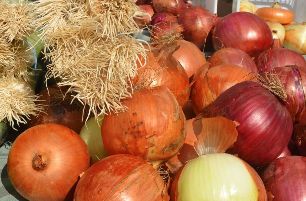 different kinds of onions as well as leeks for sale at an outdoor market