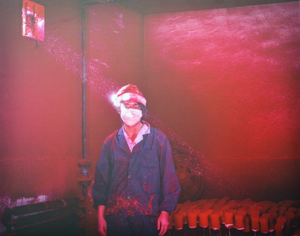 A picture of a photograph taken in a red room of a young man wearing a Santa Claus hat and a blue jacket. 