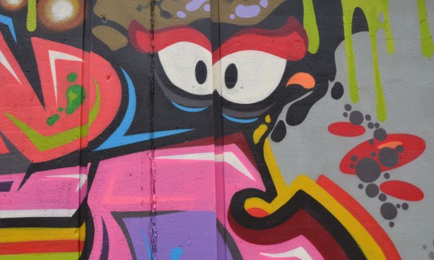 part of a larger painting on an underpass wall, eyes looking out, surrounded by many colours and shapes