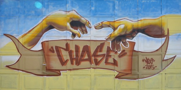 mural on a garage door, of two hands reaching for each other, in the style of Michaelangelo, with the word Chase written below on a brown banner. 