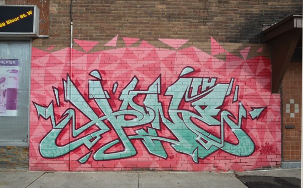 light blue geometric lettering graffiti on a background of two toned pink triangles. 