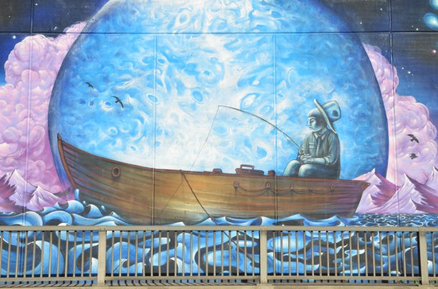 part of a larger mural, a boy is sitting at the back of a large wood boat, he is fishing, the boat is in a large bubble