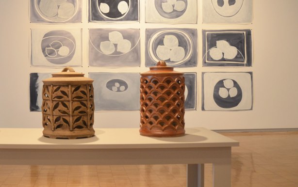 Two intricately designed ceramic containers on a table in front of a series of pictures of lemons in a bowl 