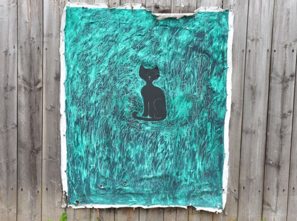 Painting on canvas stapled to a wood fence. A black silhouette of a cat that is surrounded by turquoise and farker blue swirls and smudges