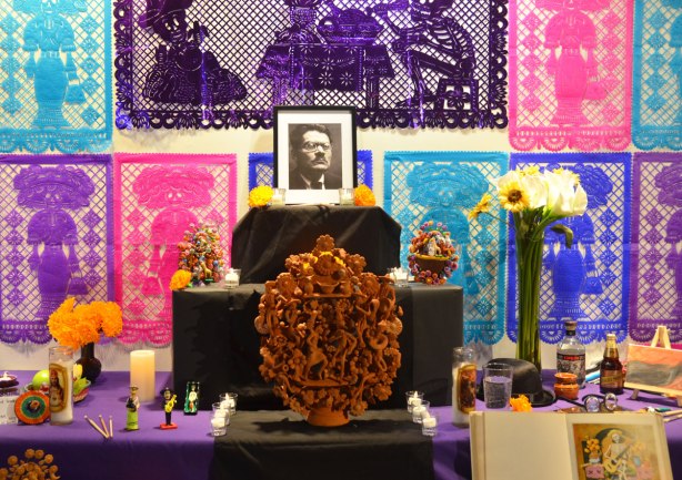 elaborate and colourful ofrenda with purple, blue and pink paper cut outs on the wall behind. 
