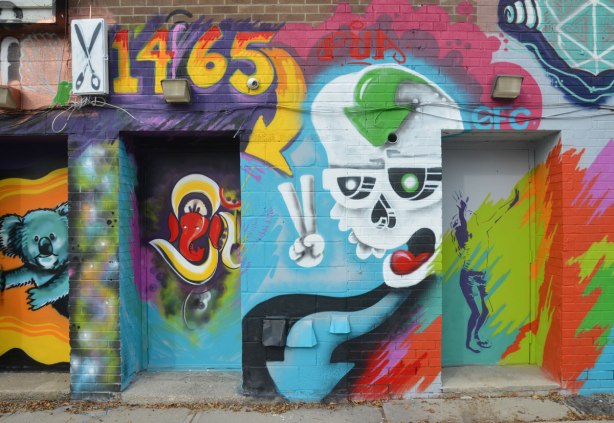 doorways behind 1465 Gerrard St. covered with street art, a white ghostly skull and a girl standing with her head back and arms upraised