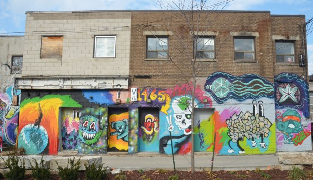 The back of a few two storey shops where the bottom half is covered with street art and murals