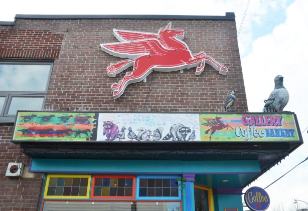 the side of the Gallery Coffee Bakery with a red winged horse sign on the upper storey of the red brick bulding. The door and window frames of the shop are painted in primary colours. 