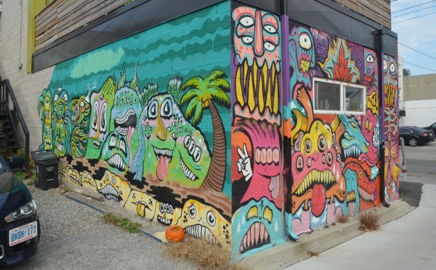 Two murals, both brightly multicoloured featuring creatures, on walls in an alley