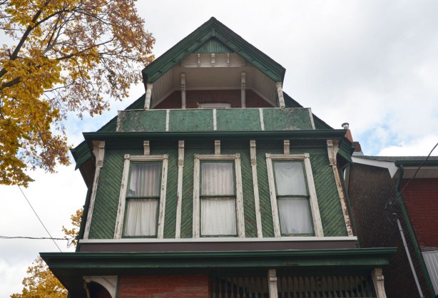 second storey wood structure protruding from house, almost the width of the house, with three vertical windows in it. A small balcony is above it. 