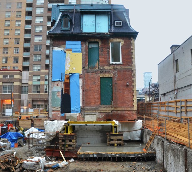 back of an old house from the 1870s, the John Irwin House, a three storey brick building, that was moved from one site to another. It is sitting on supports at the edge of a construction site. 