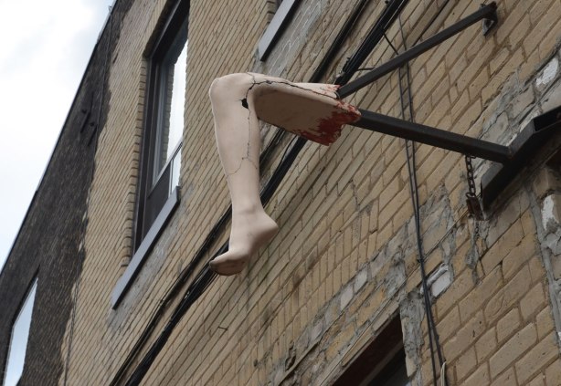 A fake leg, bent at the knee, with fake blood along the top of the thigh, attached to a wall over a door, the leg protrudes from the wall. 
