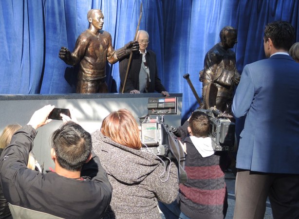 George Armstrong stands beside the statue of himself while reporters and others take pictures. 