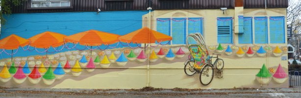 mural in Little India of a decorated bicycle in front of a beige building with orange umbrellas on the left