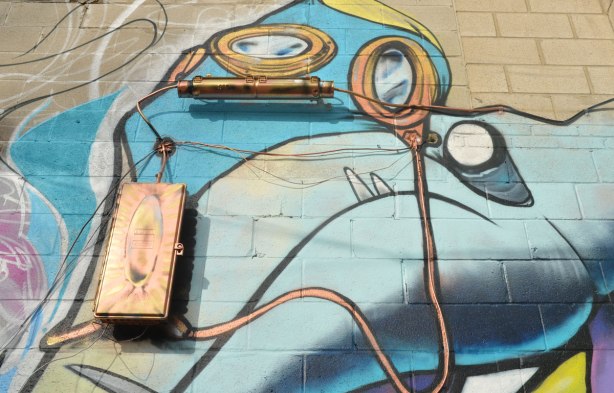 Close up of part of a larger street art painting. The metal parts of the building have been spray painted shiny gold and incorporated into the mural. 