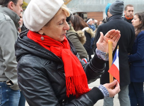 A woman in a white beret and red scarf is holding a lit candle and a small French flag