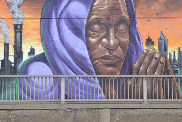 mural of a person praying, hands together, eyes closed, wearing a purple shawl over their head