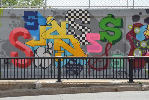 part of a large collection of street art paintings on a wall of a railway underpass on Bloor St. West as seen from across the street,