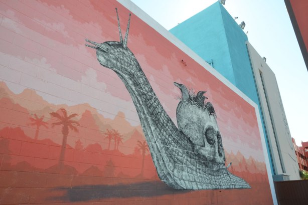 large mural of an elaborately drawn black and white snail crossing a desert. Instead of a shell on its back it has a skull. 