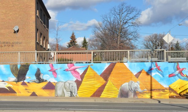 mural by Essencia Art Collective of golden pyraminds with elephants walking amongst them and eagles and macaws flying above them.