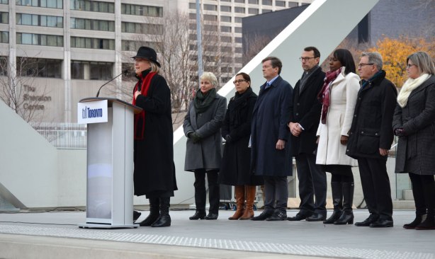 Carolyn Bennett, Liberal MP, speaks at a gathering at Nathan Phillips Square that pays tribute to the city of Paris. A lineup of other people waiting to talk, including John Tory, mayor, is standing behind her. 