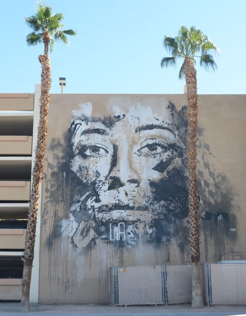 A large man's face on the side of a parking structure, with two tall palm trees