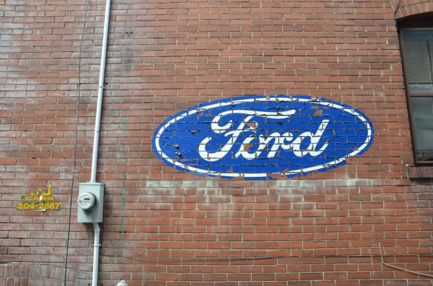 red brick wall, side of a house, with a loarge blue and white Ford logo on it. 