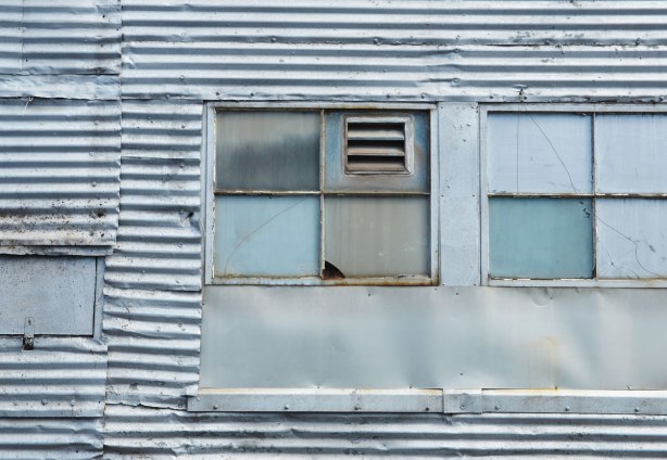 An old corrugated metal building with a window insert that has been filled in except for a small vent. 