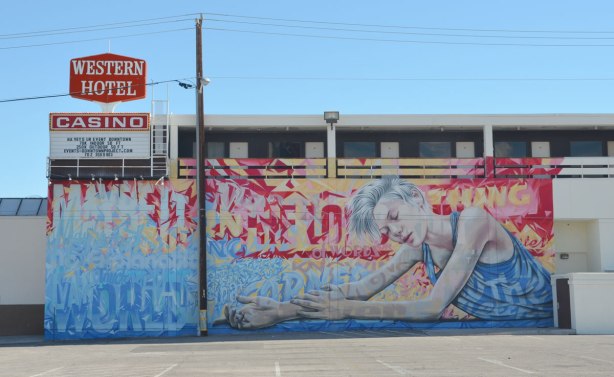 mural on the side of the WEstern Hotel and casino, a woman is sitting, eyes closed, arms outstretched in front of her. 
