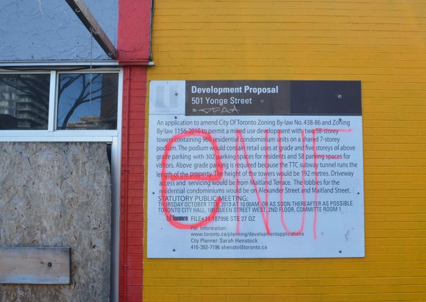 development proposal sign on a yellow wall that someone has written enuf on in big pink letters