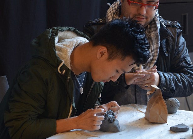 A young man carefully adds tiny clay roses to a clay skull that he has made. 