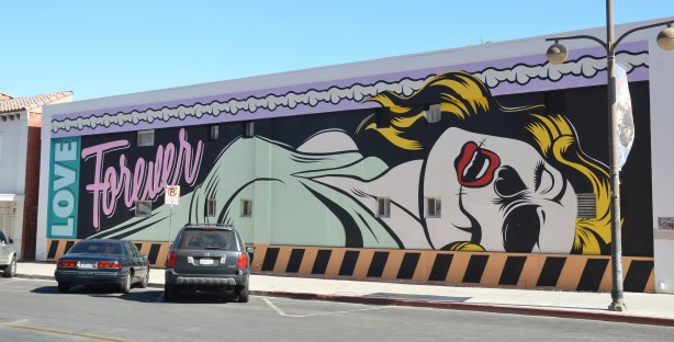 A Roy Lichtenstein-esque painting of a woman lying on her back from the waist up. Black eye, mouth open, eyes closed, blonde, pale green v-neck top