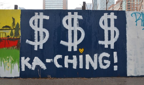 A wood plywood fence painted blue. Someone has painted three large white dollar signs on as well as the word ka-ching. 