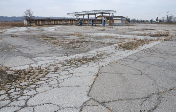 Cracks in the pavement and weeds growing up through the cracks in front of an old fuel station and motel on the QEW