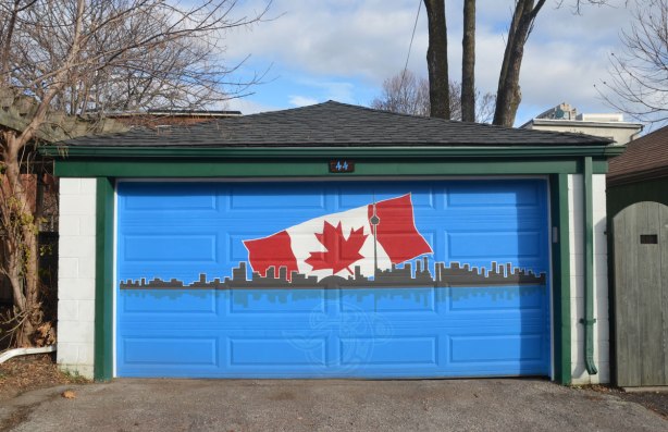 painting on a bright blue garage door of the Toronto skyline with a large Canadian flag behind ithe skyline