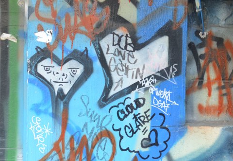 graffiti street art in an alley - Two black and white hearts, one with a face drawn on it. The words cloud + glare = [heart]