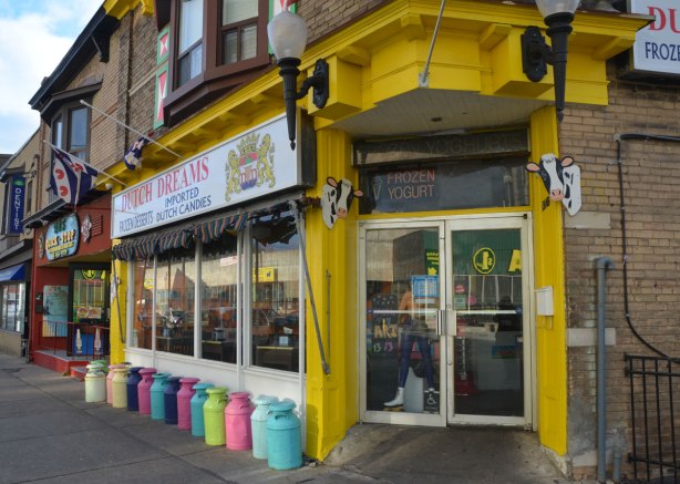 bright yellow entranceway, a line of different coloured milk cans along the exterior wall, sign says Dutch Dreams, candy and ice cream. 