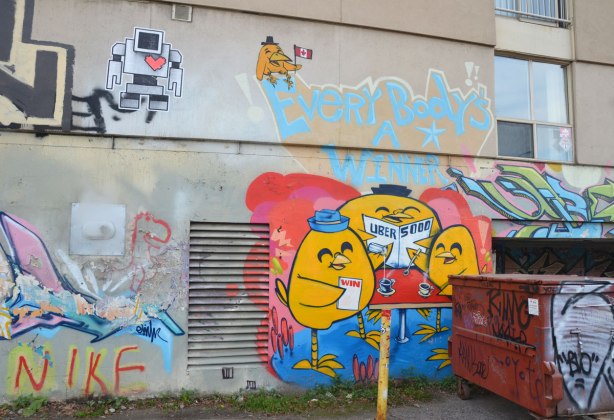 graffiti street art in an alley - a mural by Uber5000 titled Everyone's a WInner. Yellow birdies sitting around a table. There is also a lovebot wheatpaste on the wall.