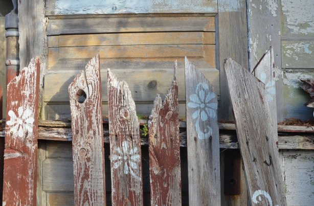 close up of old picket fence that is falling aoart, and a fence made of doors that is behind it. 