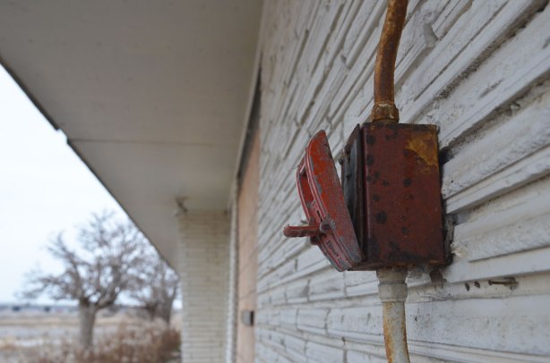 broken red fire alarm on an exterior wall. The front as come loose and it looks like the alarm was pulled 