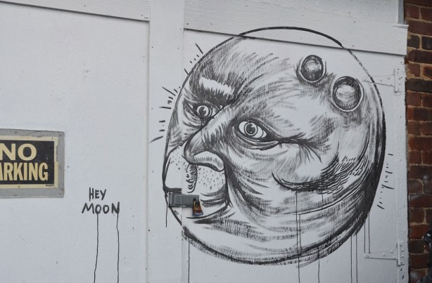 black line drawing on a white garage door in an alley. Round moon shape witha face in the moon. 
